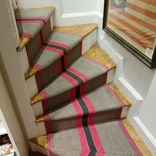 Bold red and black central stripes with natural and charcoal special weave background with red stripes on each edge. Shown here installed on a curved staircase with pie shaped steps and mitered corners.